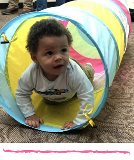 child with brown skin and curly hair crawling out of a collapsible play tunnel